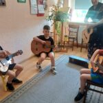 Chłopcy pod okiem nauczycielki Szkoły Muzycznej uczą się pierwszych akordów granych na gitarze