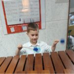 Przedszkolak stoi przy ksylofonie drewnianym i próbuje na nim grać pałeczkami