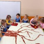 Dzieci siedzą przy stoliku i malują drzewo