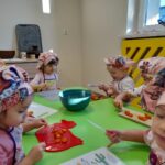 Zdjęcie przedstawia dzieci siedzące przy stoliku i krojące składniki na śląski szałot.