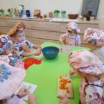 Zdjęcie przedstawia dzieci siedzące przy stoliku i krojące składniki na śląski szałot.