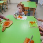 Zdjęcie przedstawia dzieci siedzące przy stoliku i krojące składniki na śląski szałot.