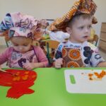 Zdjęcie przedstawia dzieci siedzące przy stoliku i krojące składniki na śląski szałot.